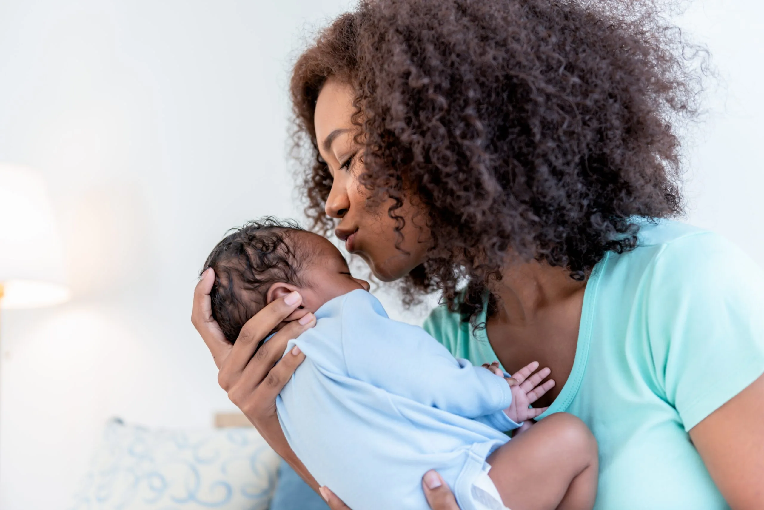 Mother lovingly holding and kissing her newborn baby, representing emotional support, postpartum care, and overnight newborn care services in Atlanta