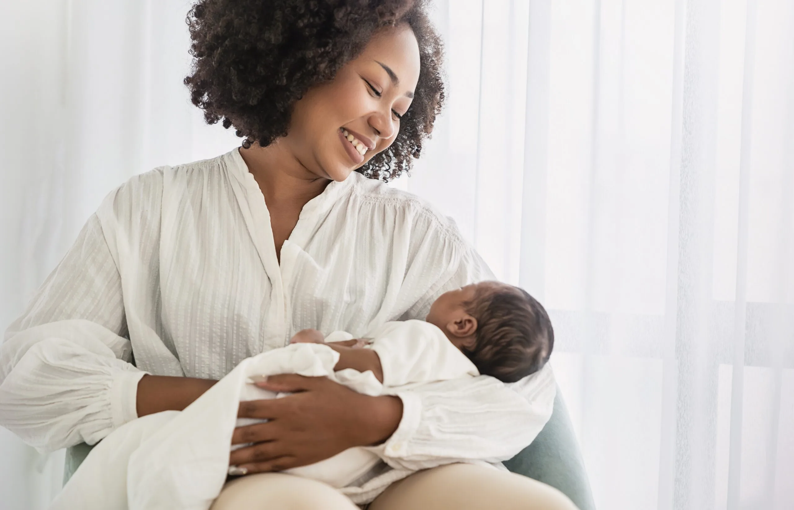 Smiling mother lovingly holding her newborn baby, showcasing maternal care and bonding.